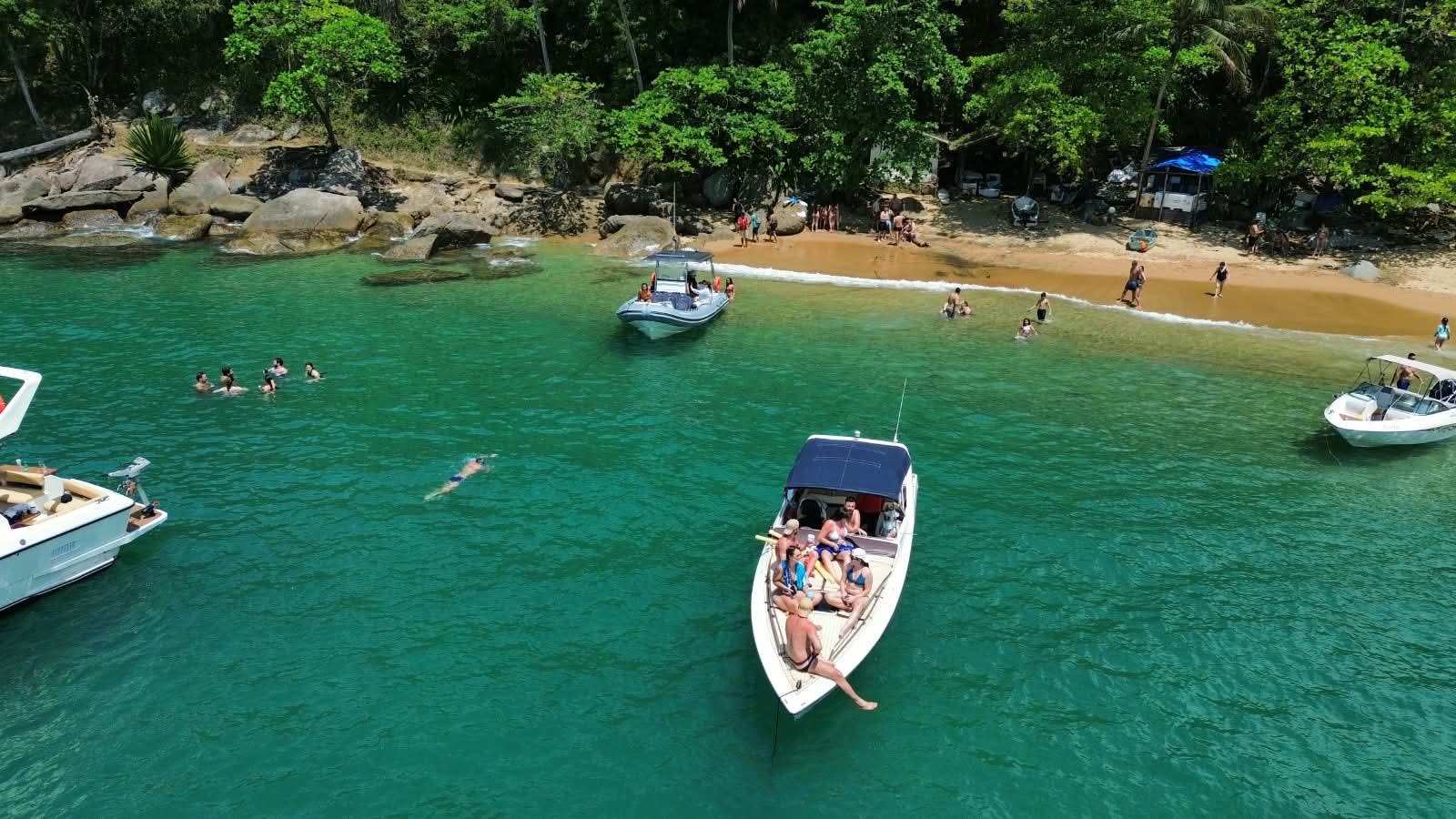 Lancha ancorada na água verde da Praia da Fome, em Ilhabela, vista de drone